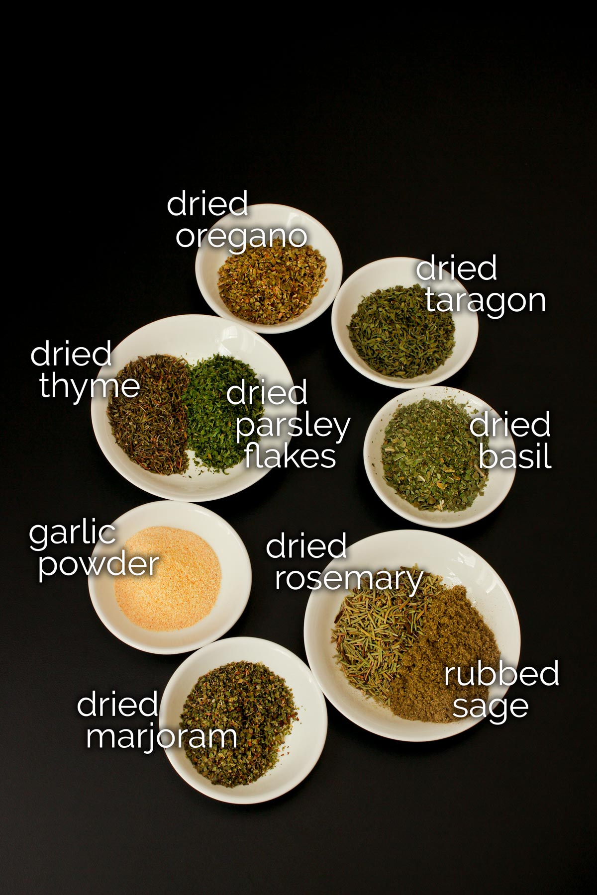 ingredients for Italian seasoning mix laid out in small white dishes on black table top.