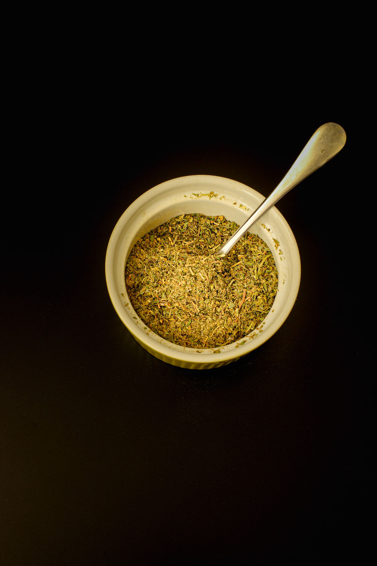 stirring Italian herbs in small bowl with demitasse spoon.