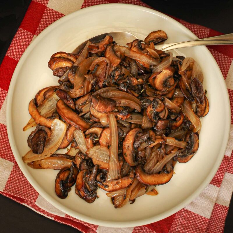 white plate of sauteed mushrooms and onions on red and white checked cloth.