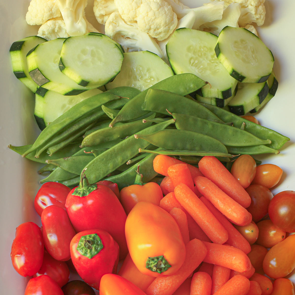 vegetable tray laid with cauliflower, cucumber, peas, peppers, and carrots.