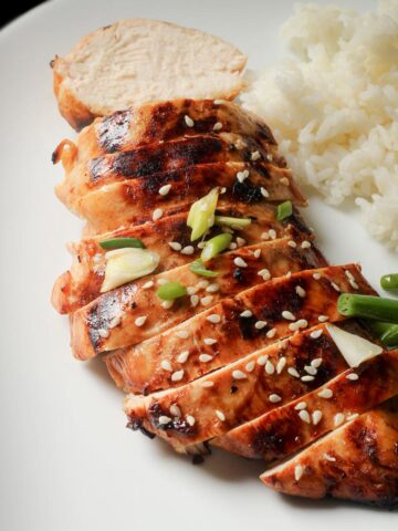 asian marinated chicken breast sliced on a plate with rice and veg.