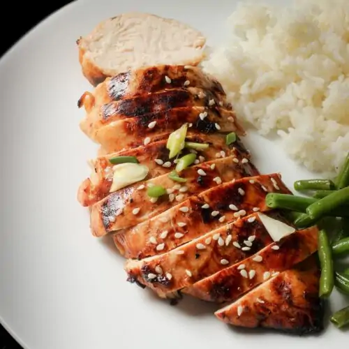 asian marinated chicken breast sliced on a plate with rice and veg.
