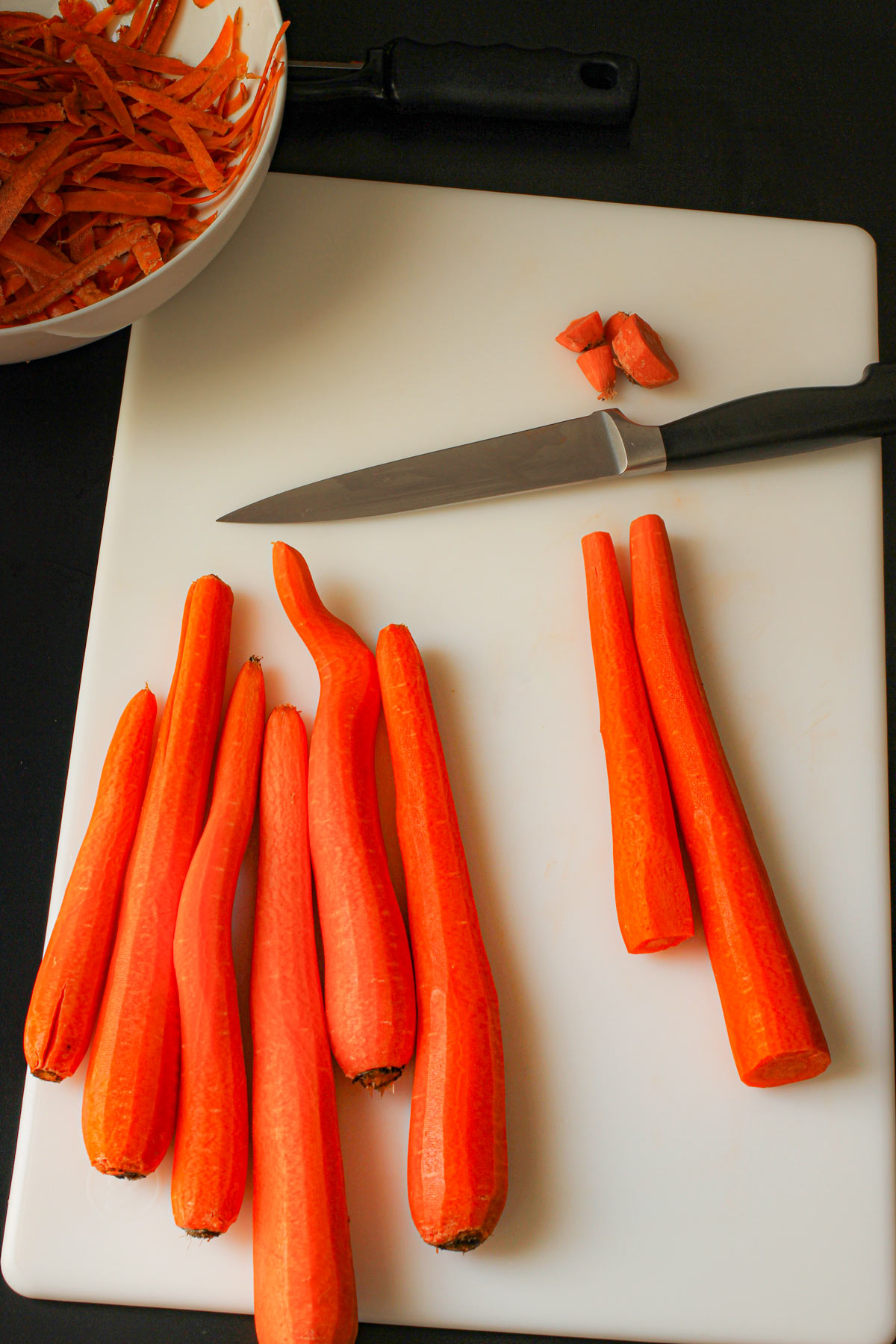 cutting the ends off peeled carrots on a white cutting board.