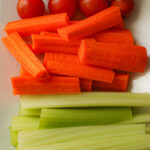 close up of carrot and celery sticks on white platter.