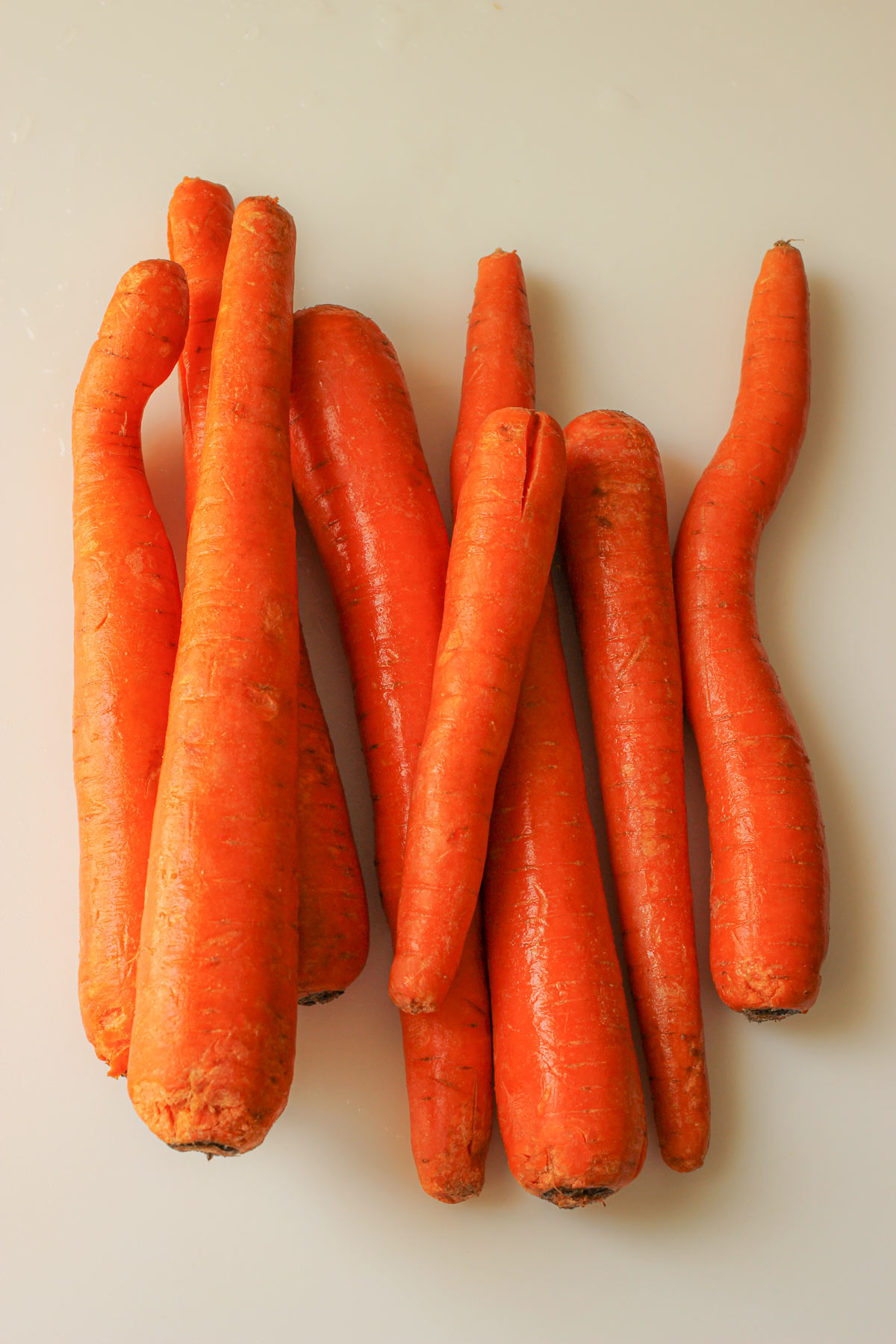 whole fresh carrots washed and laid out on a cutting board prior to peeling.