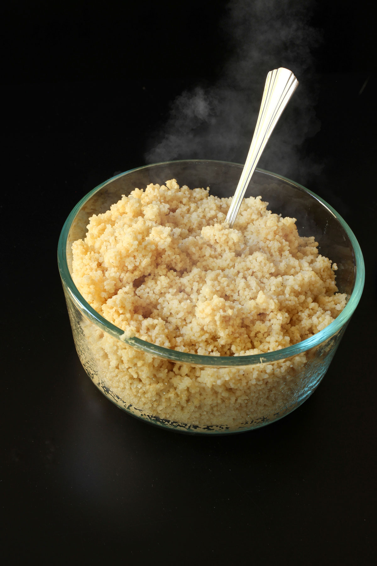 cooked couscous in a glass bowl with a fork.