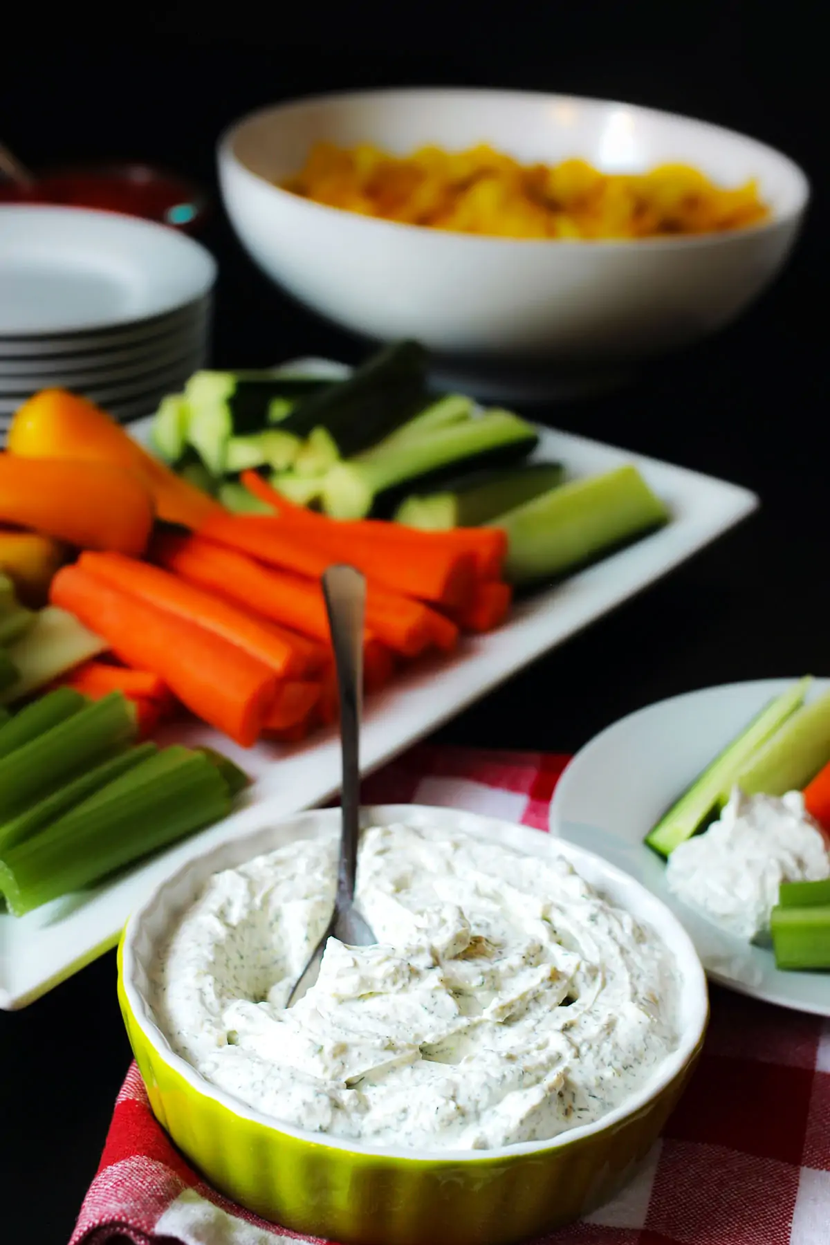 dill dip in green dish on table with platters of veggies and chips.