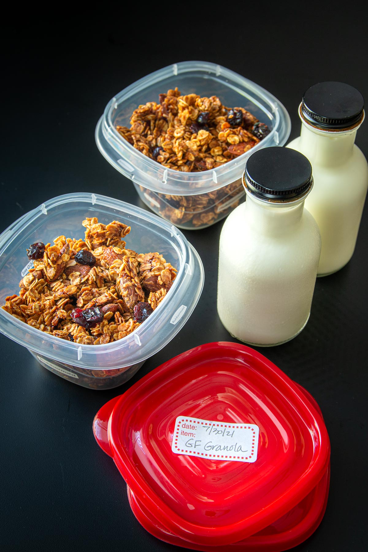 granola in meal prep boxes next to bottles of milk for packing.