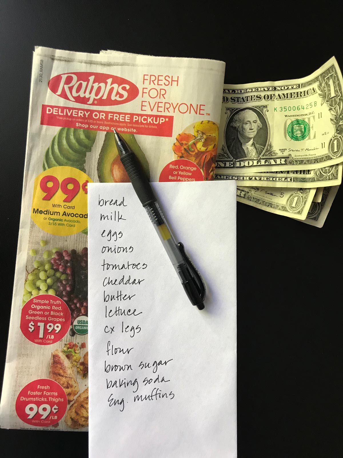 folded grocery ad next to list, cash, and pen.