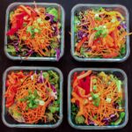 array of four square glass dishes with meal prep salads on black table top.