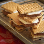 stack of smores on a broiler tray on a red cloth.