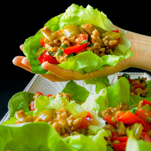hand holding a turkey lettuce wrap over a platter of wraps.