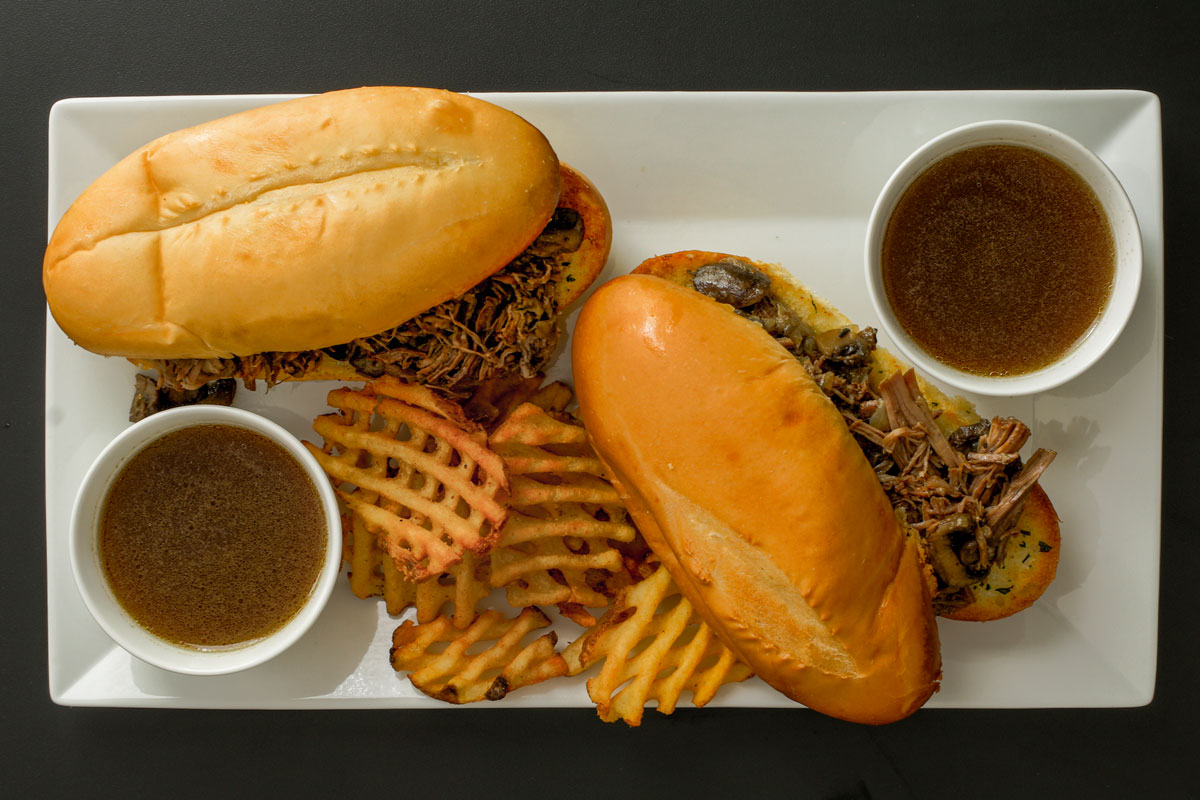 platter of french dip sandwiches with two cups of jus and waffle fries.