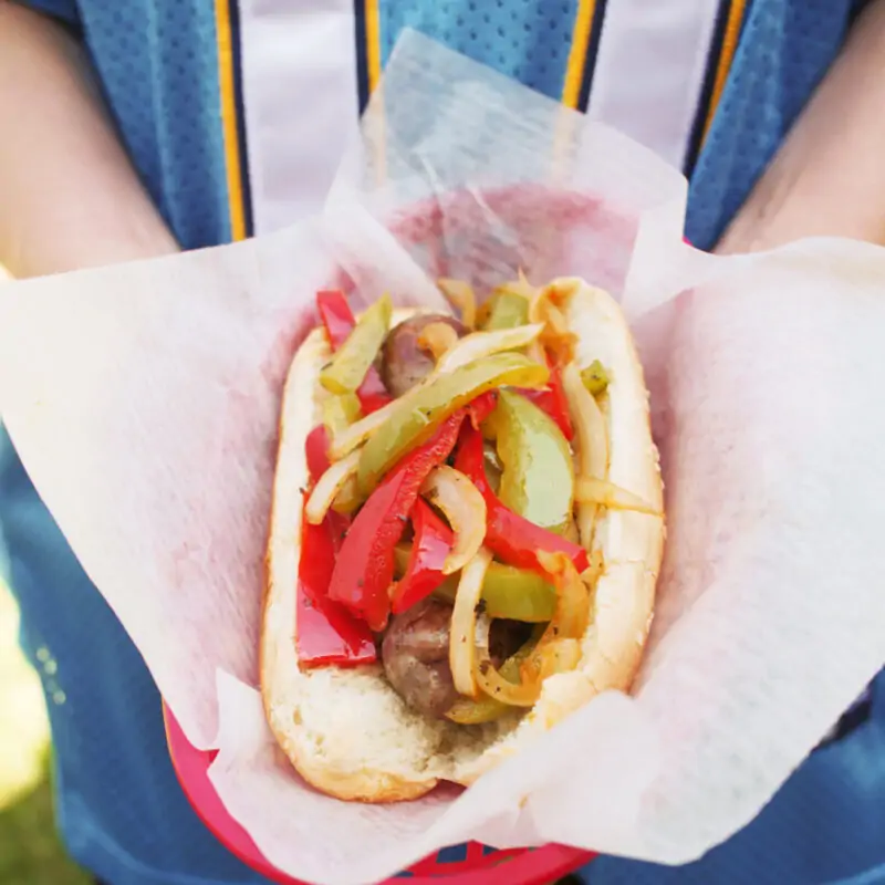 woman in chargers jersey holding basket with grilled brat in bun.