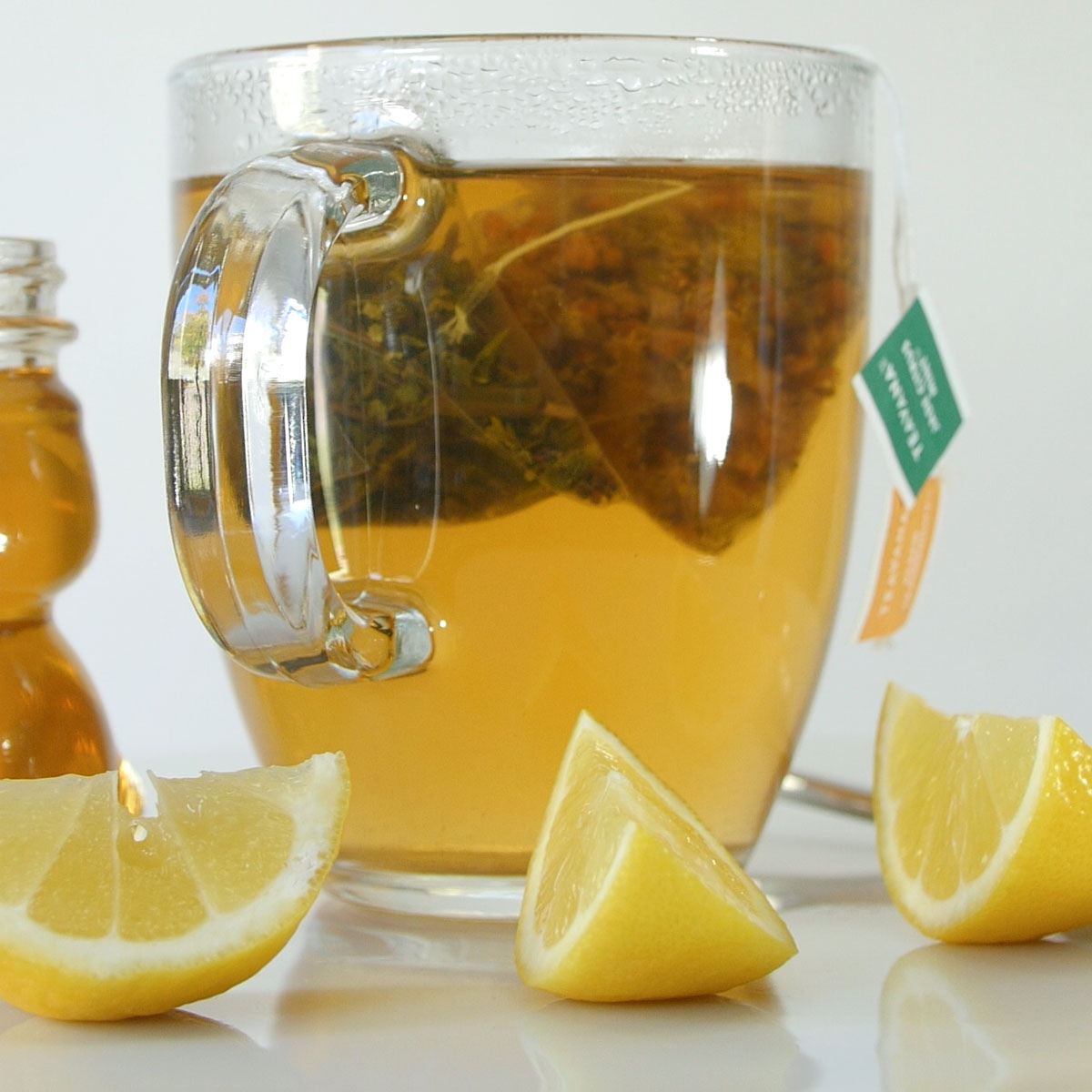 glass mug of tea next to sliced lemons and small honey bear jar.