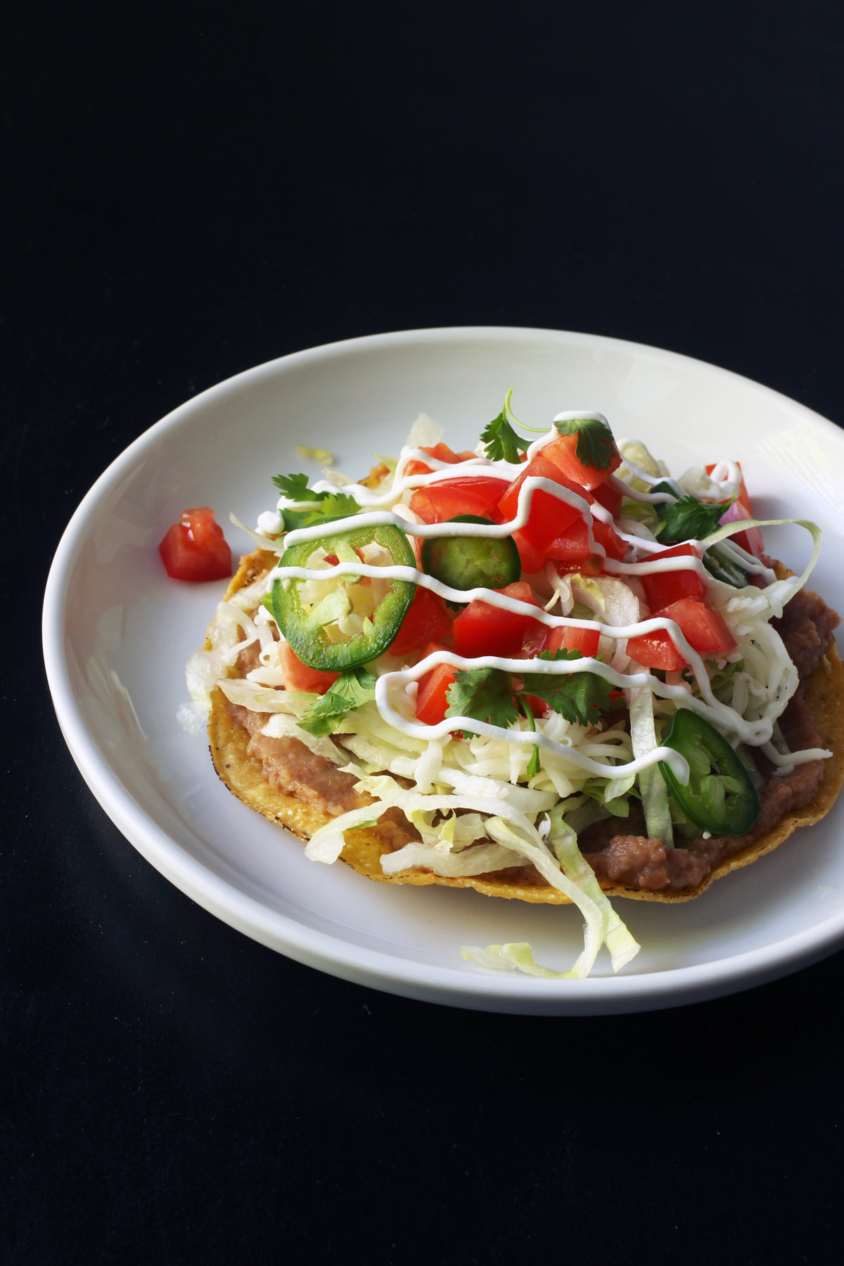 tostada with refried beans as the bottom layer on a white plate.