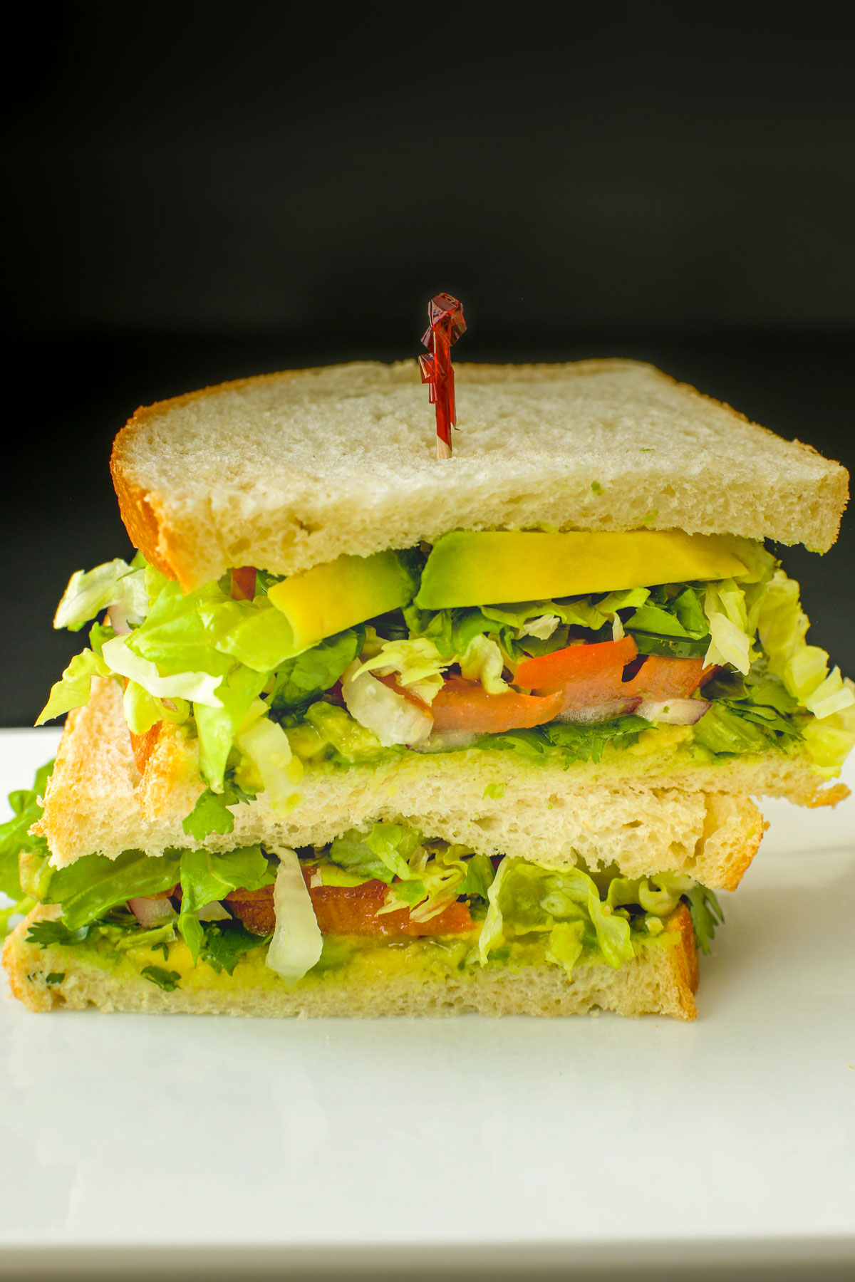 vegan sandwich with avocado cut in half and stacked on a white platter.