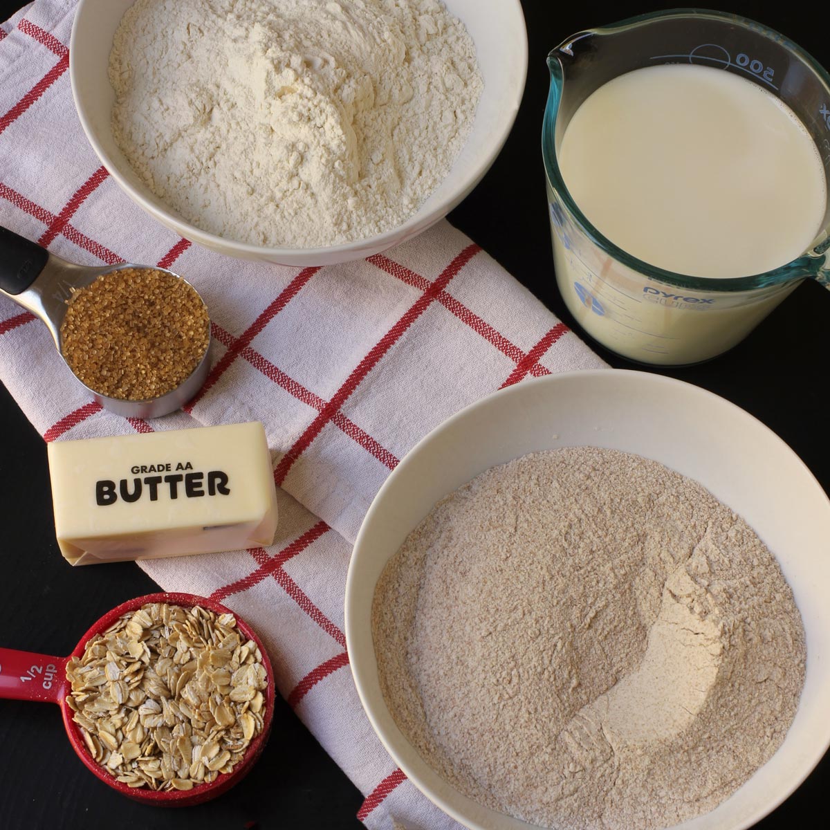 flatlay of baking ingredients on black table with red plaid cloth.