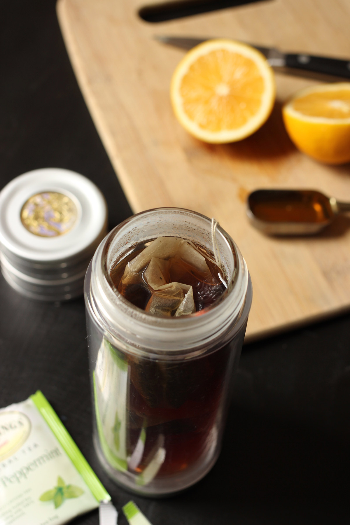 brewing tea in a travel tumbler next to honey spoon and lemon on cutting board.