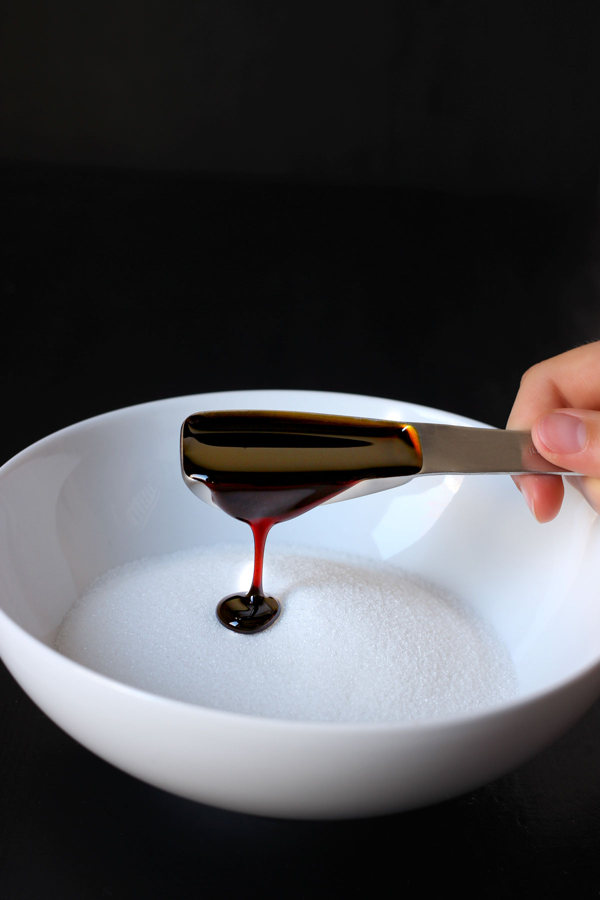 pouring molasses into a bowl of white sugar.
