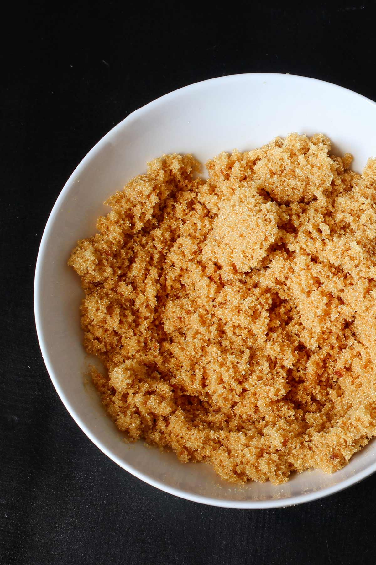 close up view of brown sugar in a white bowl on a black top.