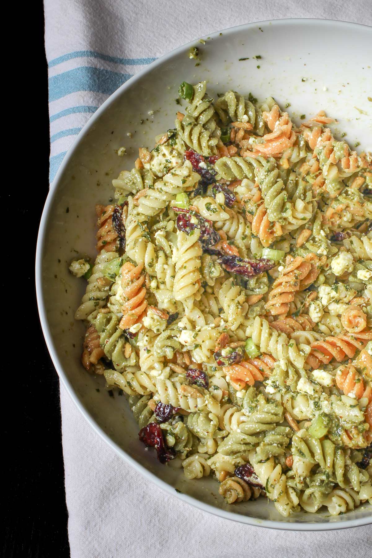 close-up view of pesto pasta salad in large white bowl on blue striped cloth.