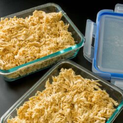 glass storage containers filled with shredded chicken next to storage lids.