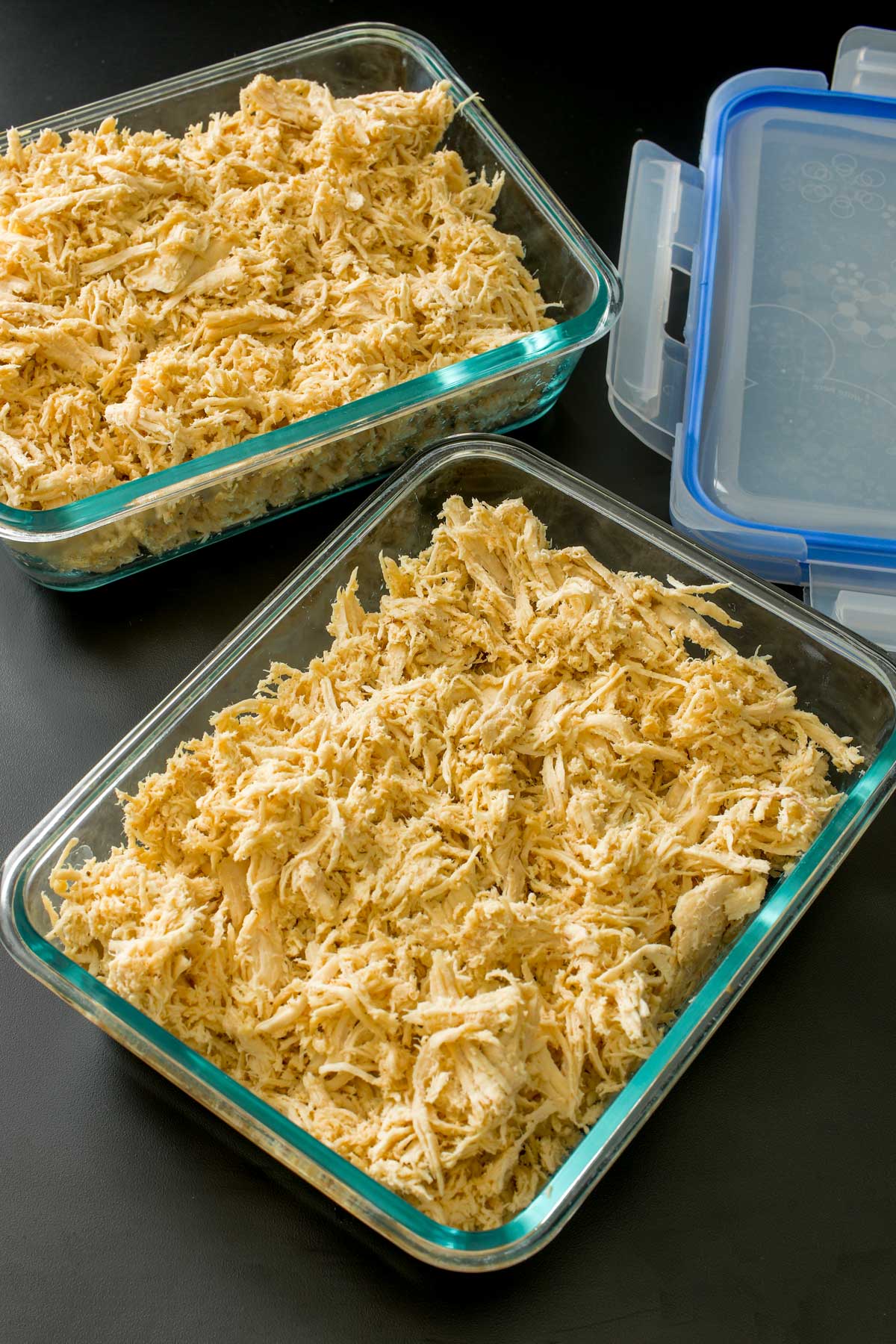 shredded chicken in glass storage containers on table next to blue lids.