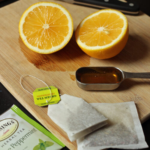 cut lemon on board next to spoon of honey and tea bags.
