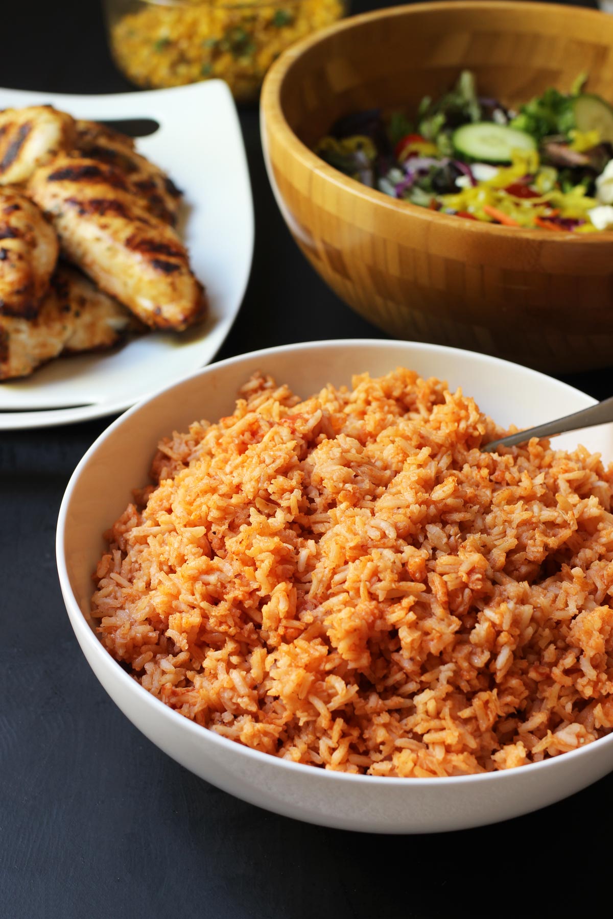 bowl of Mexican rice on dinner table with salad and chicken.