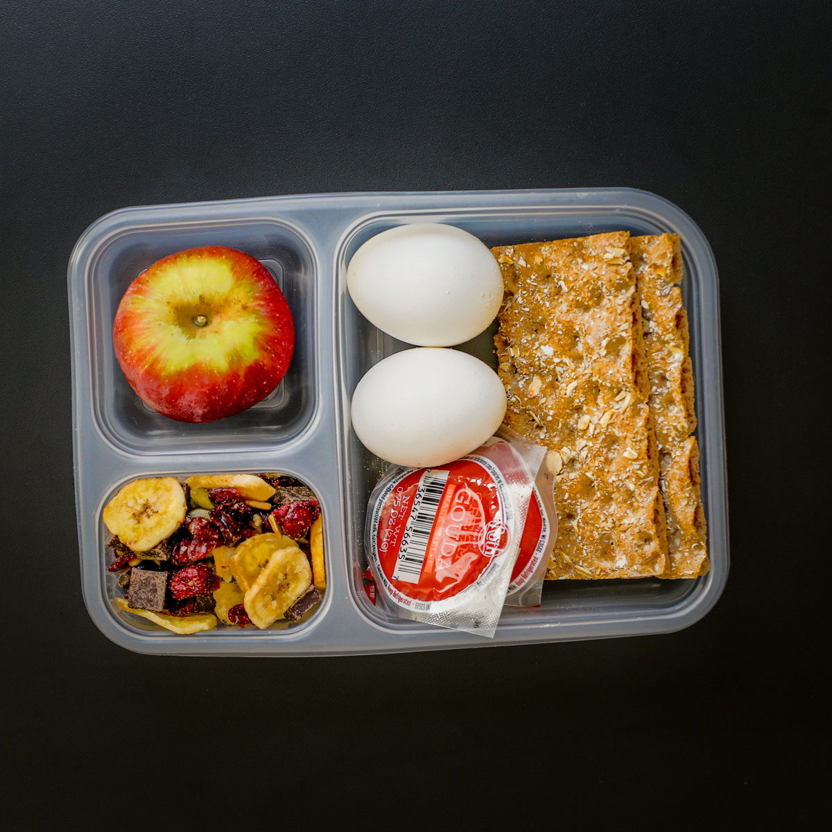 divided lunch tray with apple, eggs, cheese, crackers, and trail mix.