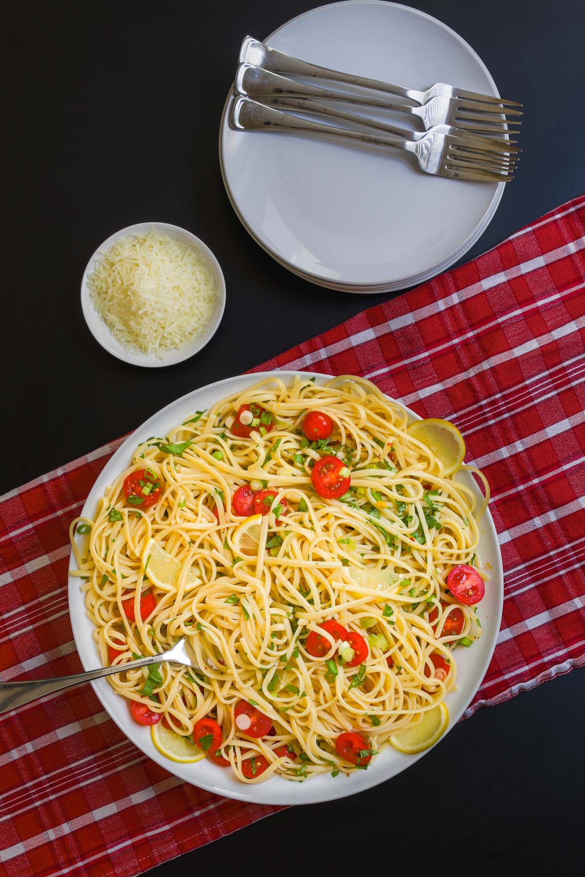 assembled pasta with lemon next to stack of plates and small bowl of cheese.