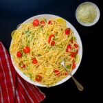 pasta with lemon and tomatoes in large platter next to red cloth and bowl of cheese.