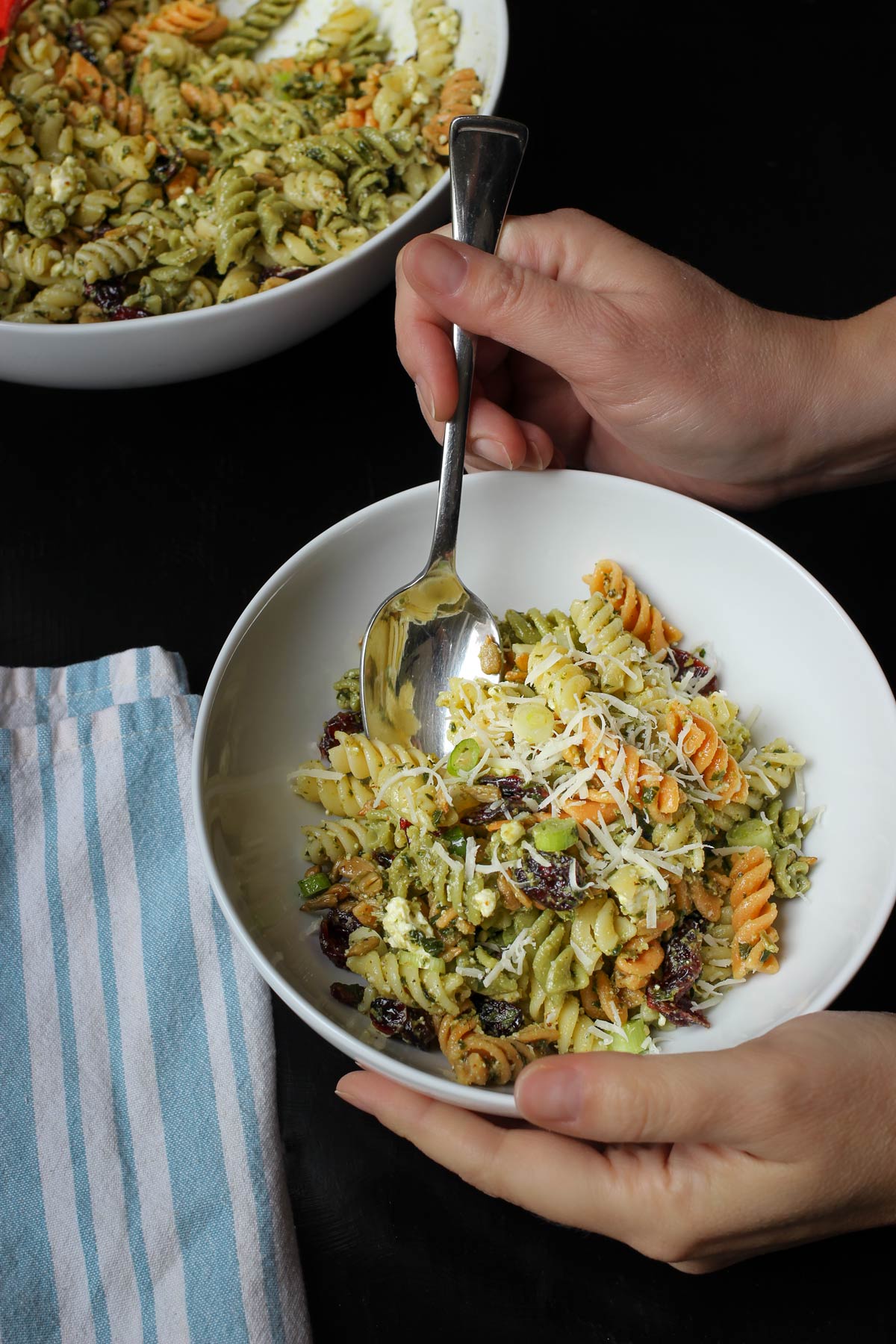 holding spoon in small bowl of pesto pasta salad.