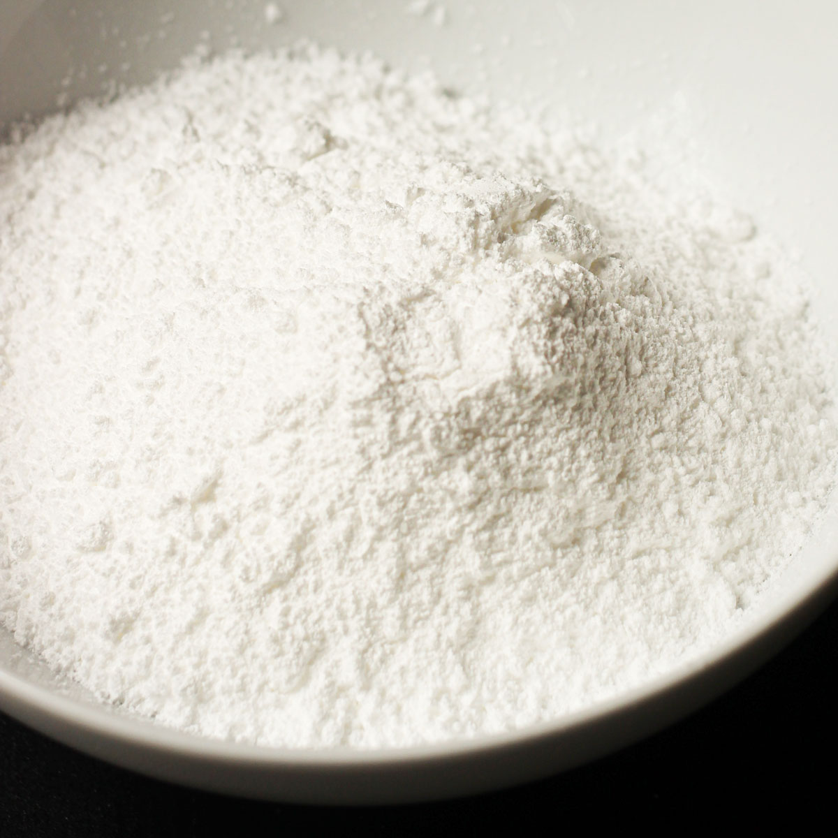 homemade powdered sugar in a white bowl on a black table top.