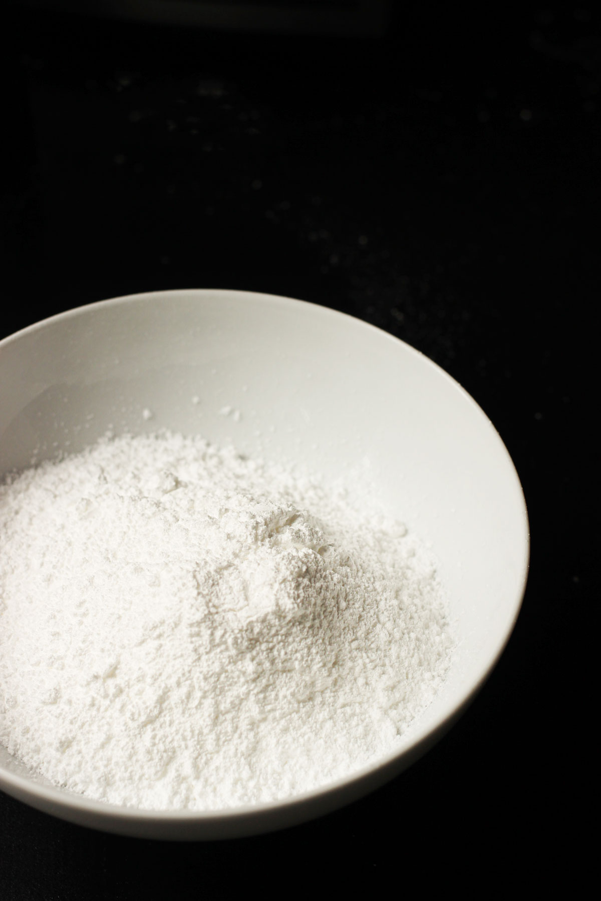 white bowl of powdered sugar on black table.