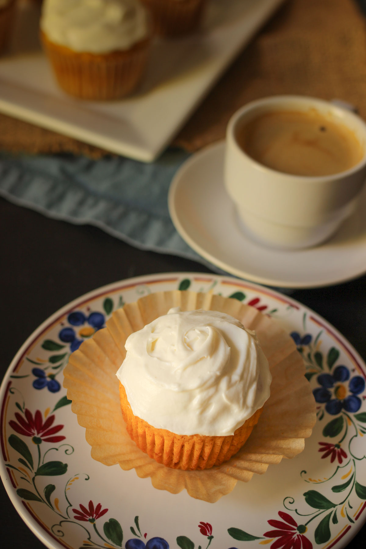cupcake sitting on open wrapper on flowered plate next to cup of espresso.