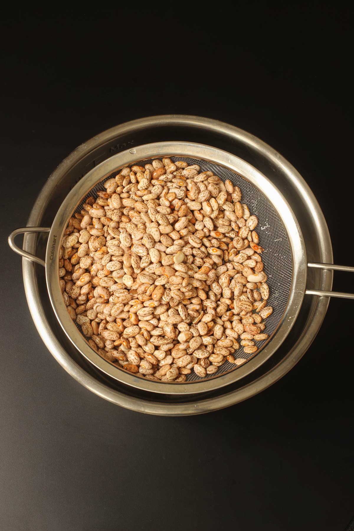 beans in fine mesh sieve draining over metal mixing bowl.