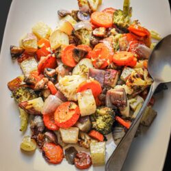 close up of roast vegetables on white platter with serving spoon.