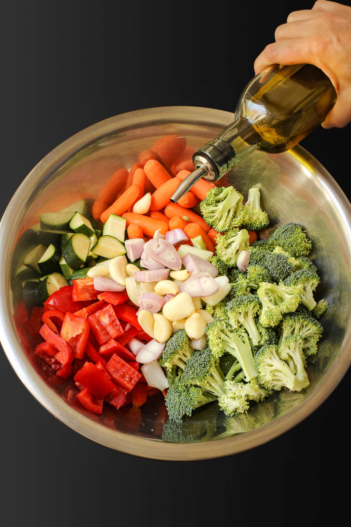 pouring oil on vegetables in bowl.