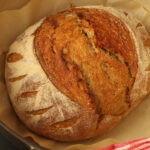 baked sourdough rye boule on paper in dutch oven.