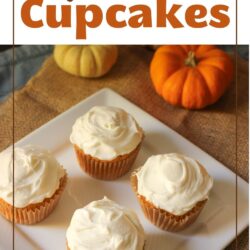 four pumpkin cupcakes on a square white platter on table with mini pumpkins.