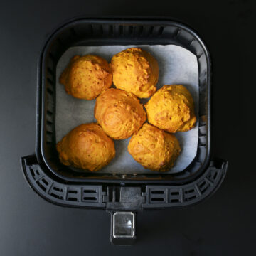 six pumpkin biscuits on parchment paper in air fryer basket.