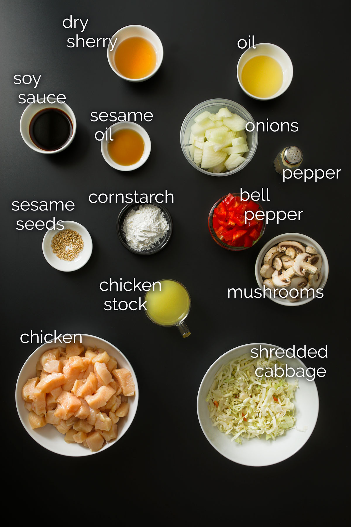 all the ingredients for chicken stir fry measured out in small bowls and dishes and laid out on a black table top.