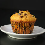 chocolate chip pumpkin muffin on white saucer in front of black background.