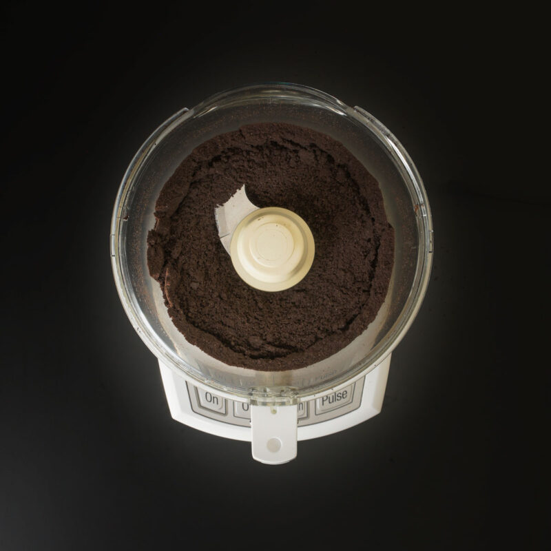 chocolate cookie crumbs in bowl of food processor fitted with metal blade.