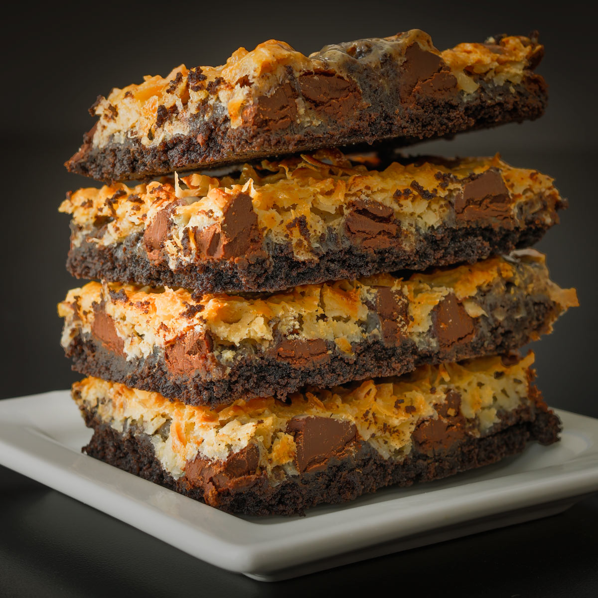 stack of chocolate coconut bars on white plate.