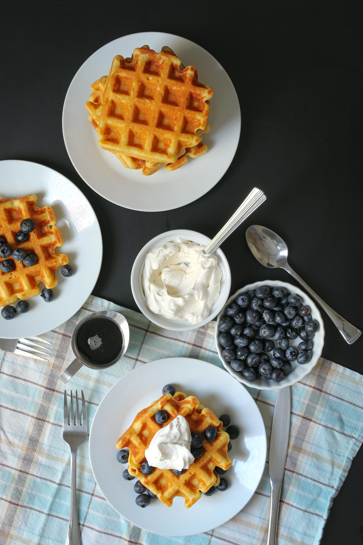 breakfast table set with waffles, syrup, whipped cream, and blueberries.