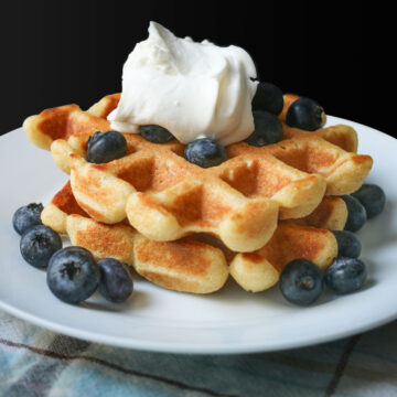 close-up of waffles stacked on a plate topped with whipped cream and blueberries.