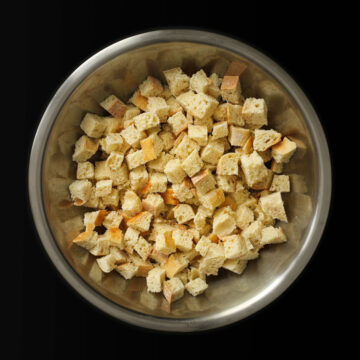 large metal bowl filled with bread cubes on black table.